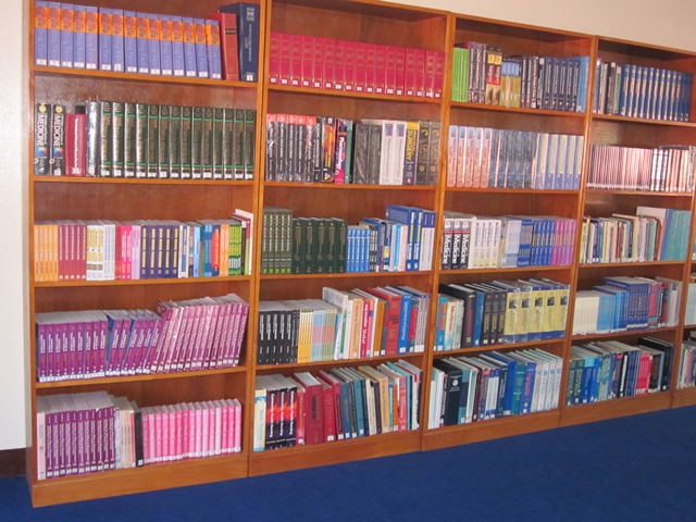 Wooden shelving filled with colorful bound books and volumes, indoor library setting, orderly mood